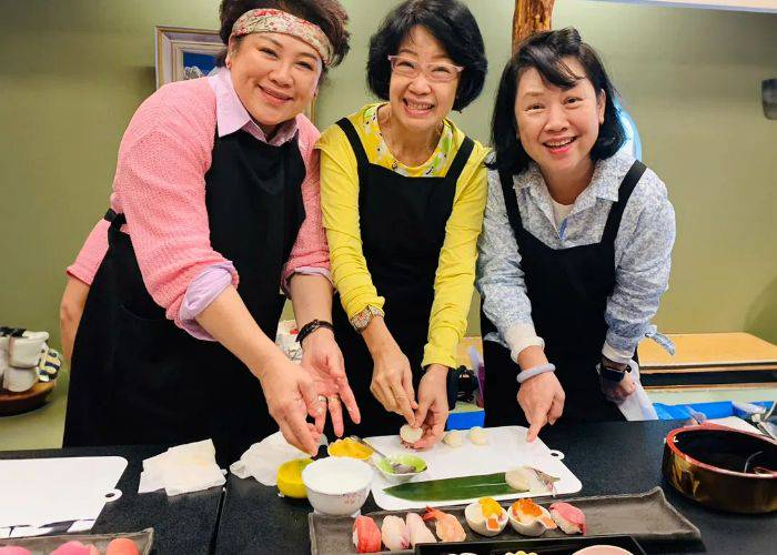 Three women smiling at the camera while making sushi at a cooking class in Niigata.